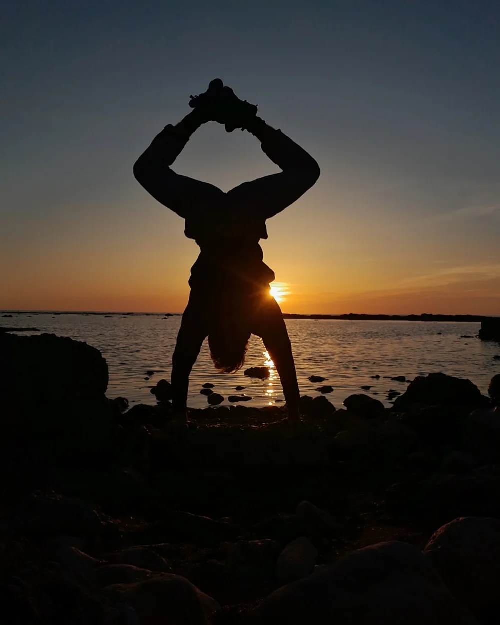 Mostafa holding a handstand on the rocks by the sea at sunset